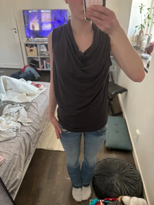 Svart ärmlös draperad topp - Snygg svart ärmlös topp med draperad halsringning som kan bäras både vanligt och offshoulder. Tunn och mjuk, perfekt till jeans eller kjol. Enkel men ändå stilren design som ger en cool vibe.