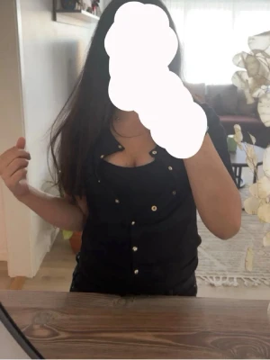 Svart kortärmad kofta med pärlknappar - Stilren svart kofta med korta ärmar och rund halsringning. Koftan har dekorativa pärlknappar framtill och är gjord i ett mjukt, ribbat material. Perfekt att bära öppen eller stängd för en trendig look.