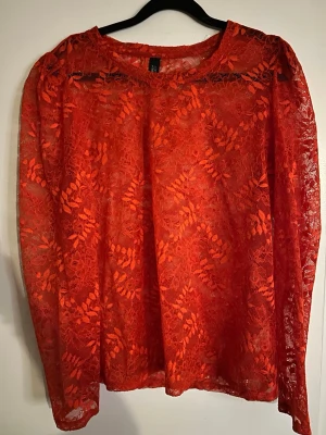 Röd spetsblus med lång ärm - Snygg röd blus i transparent spets med blommigt mönster. Blusen har långa ärmar och rund halsringning. Perfekt för dig som vill sticka ut med en trendig och feminin look. Materialet är lätt och luftigt, vilket ger en cool vibe.