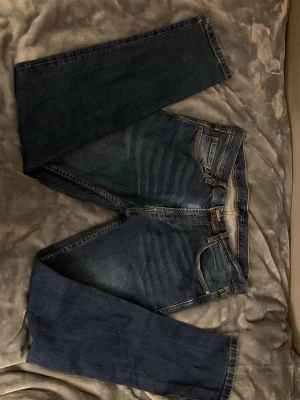 vintage mörkblå raka jeans - Säljer ett par mörkblå jeans med raka ben och klassisk femficksdesign. Jeansen har kontrastsömmar och subtila slitningar framtill för en avslappnad look. Passar perfekt till en casual outfit och är tillverkade i denim med bomullskänsla.