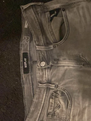 Gråa Replay jeans med smal passform - Säljer ett par gråa jeans från Replay med smal passform och klassiska fem fickor. Jeansen har snygga slitningar och detaljerade sömmar på bakfickorna. Perfekta för dig som gillar en stilren och trendig look.