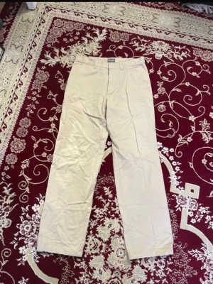 Beiga FRIDAY Chinos  - Snygga beiga chinos från FRIDAY med raka ben och klassisk passform. Byxorna har bälteshällor och stängs med dragkedja och knapp. Perfekta för en clean och avslappnad stil. 100% bomull. 2 för 120 kr på alla herrbyxor. 