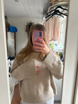 Beige oversized polotröja stickad - Mysig beige stickad polotröja med oversized passform och breda ribbade muddar vid ärmslut och nederkant. Tröjan har en hög, viktbar polokrage och är perfekt för kalla dagar. Materialet ser ut att vara mjukt och tjockt, vilket ger en avslappnad look.