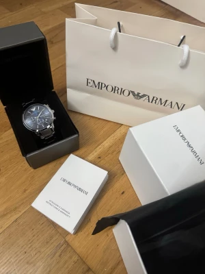 Emporio Armani silverklocka blå  - Stilren klocka från Emporio Armani med blå urtavla och silverfärgad länk i metall. Klockan har kronograf-funktion och datumvisning. Kommer i originalbox med manual och presentpåse. Perfekt accessoar för dig som gillar klassisk men modern stil.