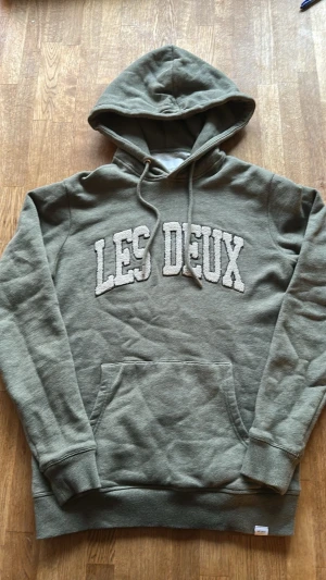 Grå hoodie från Les Deux - Snygg grå hoodie från Les Deux med stor vit broderad logga på bröstet. Mått finns