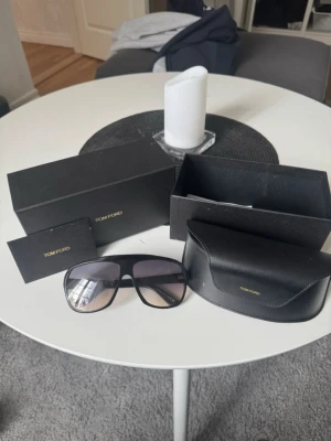 Svarta Tom Ford solglasögon - Snygga svarta solglasögon från Tom Ford med stor, rektangulär form och mörka tonade glas. Kommer med originalfodral och box. Perfekta för dig som vill ha en stilren och exklusiv accessoar till sommaren. 