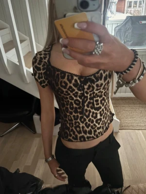 Leopardmönstrad croppad topp - Snygg croppad topp med leopardmönster och korta ärmar. Toppen har en liten rosett framtill och svarta spetsdetaljer längs halsringningen. 