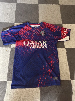PSG Neymar Jr matchtröja blå/röd - Säljer en officiell Paris Saint-Germain matchtröja från Nike med Neymar Jr och nummer 10 på ryggen. Tröjan är blå med röda och rosa grafiska detaljer, har Qatar Airways som sponsor och PSG-logga på bröstet. Perfekt för dig som älskar fotboll och PSG.