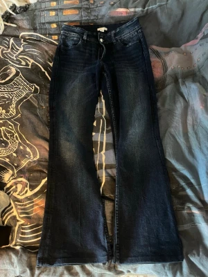 Mörkblå bootcut jeans från Gina Tricot - Säljer ett par mörkblå bootcut jeans från Gina Tricot (de är från Gina Young i storlek 170) med klassisk femficksmodell och snygga slitningar framtill. Jeansen har hög midja, dragkedja och knappstängning samt bälteshällor. Perfekta för en trendig och avslappnad look.