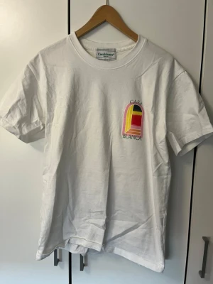 Vit t-shirt från Casablanca - Vit t-shirt från Casablanca med färgglatt tryck på bröstet i rosa, gul, röd och svart. Klassisk passform och rund halsringning. Perfekt för dig som gillar stilrena plagg med en twist.
