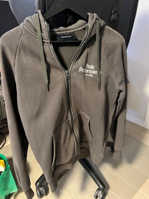 Ziphoodie från Peak Performance - Ziphoodie från Peak Performance med dragkedja, huva och snören. Fodrad insida i mjukt material och två stora fickor framtill. Logotyp broderad på bröstet. Perfekt för en avslappnad och cool look.