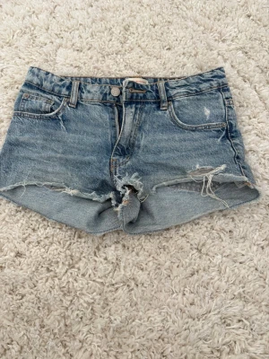 Blå jeansshorts från Gina Tricot - Säljer ett par klassiska blå jeansshorts från Gina Tricot x Izaandelle! Shortsen har vit målarfärg vid gylfen som går att se på bild 4 men annars inga defekter! Shortsen är i storlek 146!