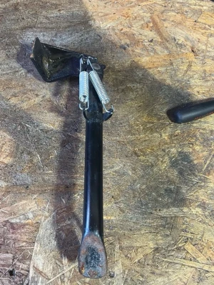 Moped stöd i svart metall - Säljer ett moped stöd i svart metall med två silverfärgade fjädrar. Stödet har en platt fot och monteringsfäste med hål för skruv. Perfekt för dig som behöver ett stabilt stöd till din moped