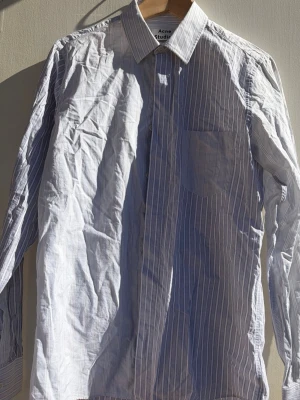 Randig skjorta från Acne Studios - Säljer en klassisk blå- och vitrandig skjorta från Acne Studios. Skjortan har lång ärm, bröstficka och knappar framtill. Tillverkad i bomull med en snygg krage och normal passform. Perfekt för dig som gillar stilrena plagg med en modern touch.