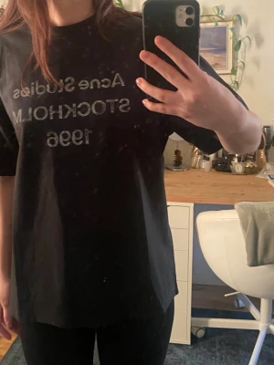 Svart Acne Studios t-shirt - Säljer en svart t-shirt från Acne Studios med tryck i vitt på bröstet där det står 'Acne Studios Stockholm 1996'. T-shirten har en loose passform och är kortärmad, perfekt för en avslappnad och trendig look.