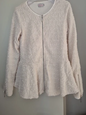 Vit strukturerad kofta med dragkedja - Säljer en vit kofta från Stockh LM med strukturerat tyg och hel dragkedja framtill. Koftan har rund halsringning, långa ärmar och lätt utsvängd passform. Perfekt för dig som gillar en stilren och modern look.