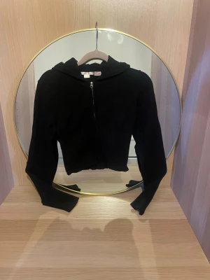 Svart cropped hoodie med dragkedja i storlek 158-164 - Säljer en svart cropped hoodie från ginatricot med dragkedja framtill och ribbade detaljer i midjan. Hoodien har långa ärmar och en klassisk huva. Perfekt för en avslappnad och trendig look.skriv för fler bilder, pris kan diskuteras!💗