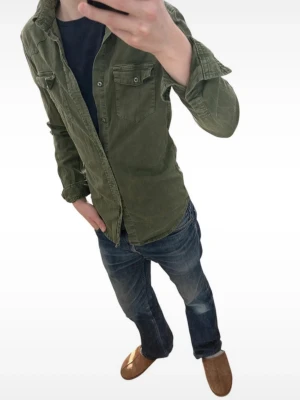Denim oliv Grön skjorta från Zara Man denim collection - Stilren grön skjorta från Zara Man Denim Collection med två bröstfickor och knappar framtill. Skjortan har lång ärm och klassisk krage, perfekt för en avslappnad men snygg look.