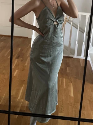 Ljusgrön långklänning från Zara - Säljer en elegant ljusgrön långklänning från Zara med smala axelband och en snygg cut-out detalj framtill. Klänningen har en figurnära passform och är tillverkad i ett glansigt, satinliknande material som ger en lyxig känsla.