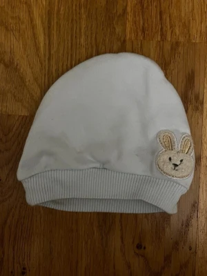 Ljusblå barn / baby mössa med kaninmotiv från Miny Kayra - Söt ljusblå babymössa med ett gulligt kaninmotiv – perfekt för att hålla din lilla varm och gosig! Varumärke: Miny Kayra. Storlek saknas, men uppskattas passa ca 0–2 månader. Säljs i mycket bra skick! Kika gärna in på mina andra annonser, jag säljer just nu flera barn- och babyplagg!