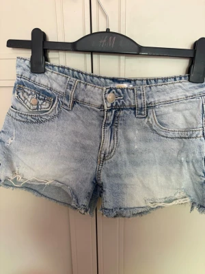 Ljusa jeansshorts med slitningar & fina fickor med design på - Snygga ljusblå jeansshorts från Gina med slitna detaljer och fransig kant. Klassisk femficksmodell med knapp och dragkedja framtill. Perfekta för sommardagar och festivaler.