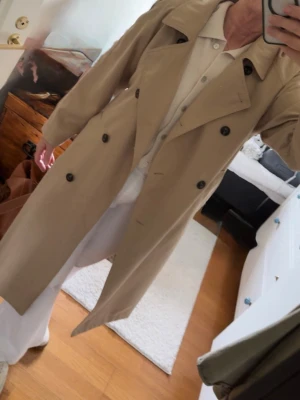 Beige trenchcoat med dubbelknäppning - Ny utan prislapp, bara provad. Nypris 559kr från Zalando i April. Stilren beige trenchcoat med klassisk dubbelknäppning och bred krage. Jackan har raka ärmar, två sidofickor och ett bälte i midjan för en snygg siluett. Perfekt för lager på lager och tidlös i garderoben. 100% Polyester . XL 
