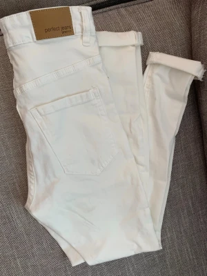 Vita jeans från Gina tricot  Perfect Jeans - Säljer ett par vita jeans från Perfect Jeans Molly med klassisk femficksdesign och rak passform. Jeansen har en snygg läderpatch bak i midjan och är tillverkade i ett mjukt bomullsmaterial. Perfekta för dig som gillar stilrena och ljusa plagg. Storlek S mini 