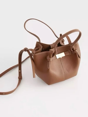 Brun bucket bag med axelrem - Snygg brun bucket bag i slätt konstläder med justerbar axelrem och två handtag. Väskan har dekorativa knutar på sidorna och ett guldfärgat spänne framtill. Perfekt storlek och den kommer från Lindex. Har använt fåtal gånger och ser helt ny ut. (Ny pris 350kr)💗💗