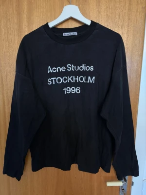 Acne Studios longsleeve - Svart longsleeve från Acne Studios med tryck 'Acne Studios STOCKHOLM 1996' på bröstet. Klassisk rund halsringning och avslappnad passform. Perfekt för en stilren och trendig look. Köpt på vinted men har kvittot från förra ägaren.