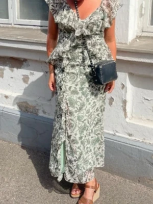 Zara Blommig långklänning med volang - Långklänning med blommigt mönster i vitt och grönt. Klänningen har v-ringning och volangdetaljer. 