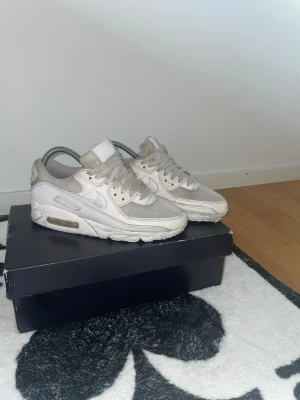 Nike Air Max 90 vita sneakers - Säljer ett par klassiska Nike Air Max 90 sneakers i vitt. Skorna är snygga men har lite defekter och och är slitna men funkar. Lite plast på sulan har gått av men inget man märker. Och inget vatten eller nåt kommer in.