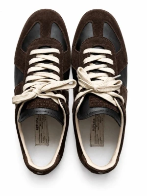 Masion Margiela Gats bruna - Snygga sneakers i svart läder med mörkbruna mockadetaljer och vita snören. Klassisk låg modell med gummisula och kontrasterande material som ger en stilren look. Perfekta för dig som gillar tidlös design och vill ha något som sticker ut lite extra.