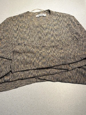 Beige stickad tröja Carin Wester - Stickad tröja från Carin Wester i storlek S. Tröjan har en melerad beige och grå färg med rund halsringning och lång ärm. Perfekt för lager-på-lager och enkel att matcha med jeans eller kjol.