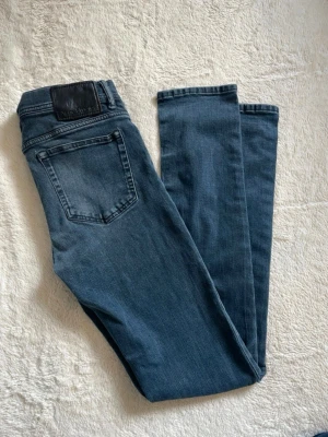 Mörkblå Acne Studios skinny jeans - Säljer ett par mörkblå skinny jeans från Acne Studios. Klassisk femficksmodell med svart läderpatch bak i midjan. Jeansen har smal passform och är tillverkade i mjuk denim med lite stretch för extra komfort.