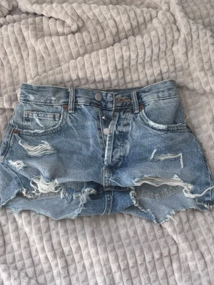 Blå midwaist jeansshorts med fransar från Zara - Säljer ett par blå jeansshorts med råa kanter och slitna detaljer framtill. Shortsen har flera fickor samt knappgylf. Shortsen är mer åt det blåa hållet. Använda ett fåtal gånger.