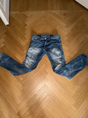 Blå slim-fit jeans från Diesel - Säljer ett par blå slim-fit jeans från Diesel, modell Shioner. Jeansen har en skinny passform och slitna detaljer med tvättade effekter. Klassisk femficksmodell med knappgylf och snygga kontrastsömmar. Perfekta för en trendig och avslappnad stil.