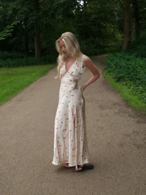 Midsommarklänning  - Superfin långklänning i ljus beige med små röda blommor. Perfekt för sommaren! Klänningen är  oanvänd med prislapp kvar. 