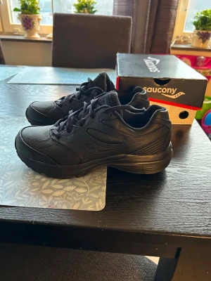 Svarta Saucony sneakers i läder HELT NYA - Stilrena svarta sneakers från Saucony i läder med klassisk låg profil och robust sula. Helt nya, enbart provade. Skorna har diskreta detaljer och Saucony-logga på sidan. Perfekta för dig som gillar en clean och sportig look. Nypris ca 1300kr.