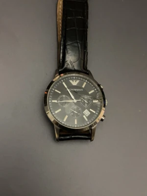 Emporio Armani Herr klocka - Säljer nu denna herr klocka från Emporio Armani. Extremt fin som du kan ha till speciella evenemang.   Däremot som du kan se på bilderna har den fått en del skada som du som köpare enkelt kan fixa, alltså glaset som du kan beställa online och ett annat läderband samt ett batteri givetvis.