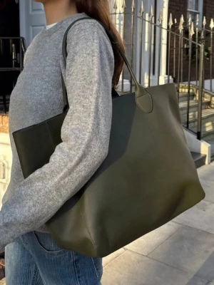 stor olivgrön shoppingväska  - Aldrig använd, kom med ett litet märke som man kan se på sista bilden men inget som märks! Stilren och rymlig shoppingväska i olivgrön skinnimitation med två långa handtag. Väskan har en enkel, slät design utan synliga loggor eller detaljer och passar perfekt för dig som vill ha en minimalistisk look. Perfekt att bära över axeln. 