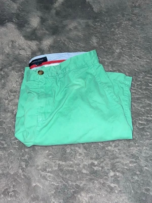 Tommy Hilfiger Mintgröna Chino Shorts - somriga chino-shorts från Tommy Hilfiger i en härlig mintgrön färg. Shortsen är gjorda i en mjuk bomullskvalitet och har en klassisk passform. De har den lilla Tommy-flaggan broderad ovanför bakfickan.  