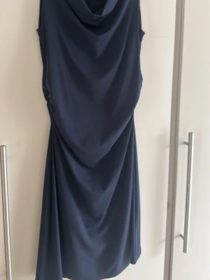 Marinblå klänning från Esprit - Säljer en marinblå klänning från Esprit med draperad halsringning och elegant fall. Klänningen är ärmlös och har en mjuk, slät polyesterkänsla som gör den bekväm och snygg. Perfekt för dig som vill ha en stilren look.