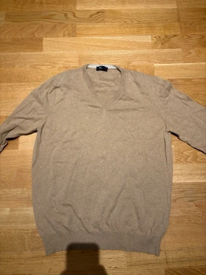 Beige stickad tröja Fiume - Klassisk beige stickad kashmir tröja från Fiume med v-ringning och långa ärmar. Tillverkad i Italien och har ribbade muddar vid ärmslut och nederkant. Perfekt för dig som gillar en enkel och stilren look. Strl L