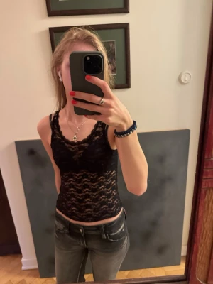 Svart spetslinne från Gina Tricot - Snyggt svart spetslinne från Gina Tricot med blommigt spetsmönster. Linnet är ärmlöst och har en tight passform som framhäver figuren. Perfekt att styla med jeans eller kjol för en trendig look. Funkar också jättefint med en kortare T-shirt över. Är i 134/140 men tycker den passar xs eller xxs 