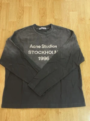 Svart långärmad topp Acne Studios - Svart långärmad topp från Acne Studios med vit text 'Acne Studios STOCKHOLM 1996' på bröstet. Rund halsringning och relaxed fit, perfekt för en clean och modern look. Tillverkad i mjuk bomull.
