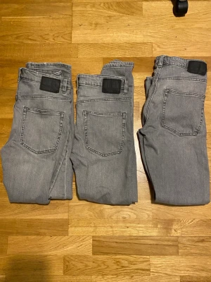 Grå jeans med raka ben - Säljer tre par grå jeans med raka ben och klassiska bakfickor. Jeansens färg är ljusgrå och de har svarta patchar vid linningen. Materialet är denim och passformen är avslappnad. Perfekt för dig som gillar en enkel och stilren look.