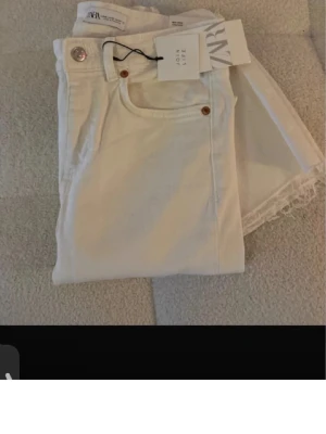 Vita raka jeans från Zara - Snygga vita jeans från Zara med raka ben och råa kanter nertill. Klassisk femficksmodell med silverfärgad knapp och detaljer i koppar. Perfekta för en clean och trendig look. Materialet är bomull för en skön känsla.kan möjligtvis sänka priset vid snabba affärer 