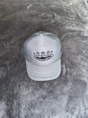 Cortiez keps - Snygg grå keps med mesh på sidorna och bak, samt broderade stjärnor och ett motiv framtill. Perfekt för en avslappnad streetstyle-look. Justerbar baktill för bästa passform.