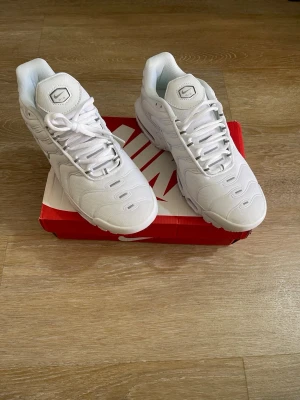 Nike vita Air Max Plus sneakers - Nike Air Max Plus sneakers i helvitt med mesh- och syntetmaterial. Klassisk chunky sula med synliga Air-enheter och vågiga detaljer på ovandelen. Swoosh-logga på sidan och logotyp på plösen. Perfekta för dig som gillar sportig och clean stil.