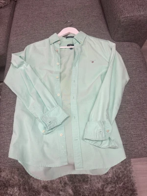 Mintgrön slim fit skjorta från GANT - Säljer en mintgrön slim fit Oxford-skjorta från GANT med klassisk krage och knappar hela vägen. Skjortan har lång ärm och diskret logga på bröstet. Perfekt för dig som gillar stilrena och fräscha plagg.